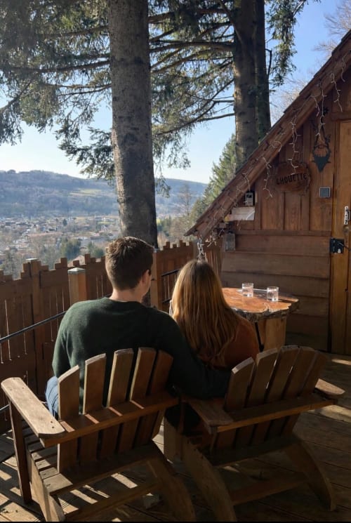Deux hôtes admirant la vue sur les montagnes depuis des chaises Adirondack en bois sur la terrasse de Cabane Chouette aux Cabanes des