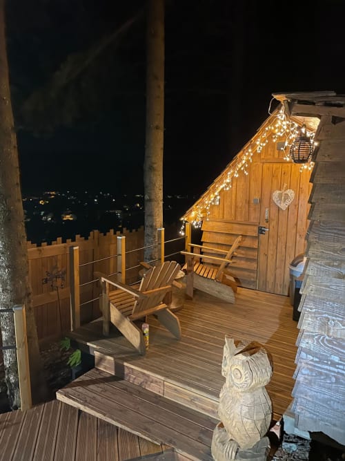 Vue nocturne de la cabane Chouette aux Cabanes des Marchous, illuminée de petites lumières, terrasse en bois