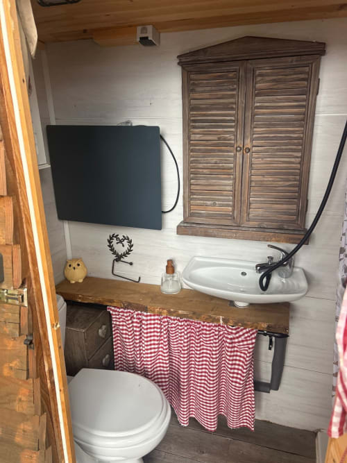 Salle de bains de la Cabane Chouette avec toilettes, lavabo mural, meuble en bois et rideau à carreaux rouges