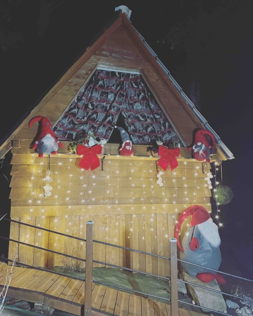 Festive wooden cottage Cabane Marmotte decorated with Christmas lights, gnomes, and red bows at Les Cabanes des Marchous in
