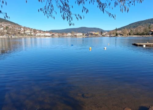 Calm lake view with moored buoys, forested mountains, and waterfront village of Granges-Aumontzey