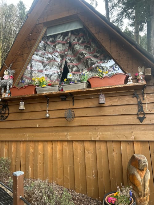 Cozy wooden cabin with peaked roof and large windows, decorated with colorful spring flowers and hanging ornaments,