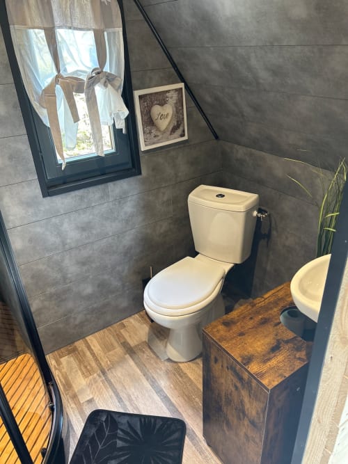 Modern bathroom in Cabane L'Écureuil cottage with white toilet, cream sink, gray tile walls, and wood flooring at Les Cabanes