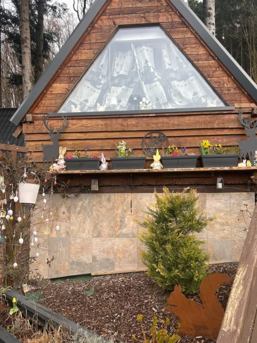 Charming wooden A-frame cottage at Les Cabanes des Marchous with triangular window, flower planters, and forest surroundings