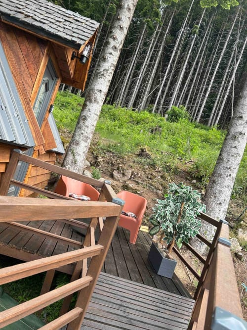 Wooden cabin deck with red chair overlooking forest, Cabane L'Écureuil at Les Cabanes des Marchous