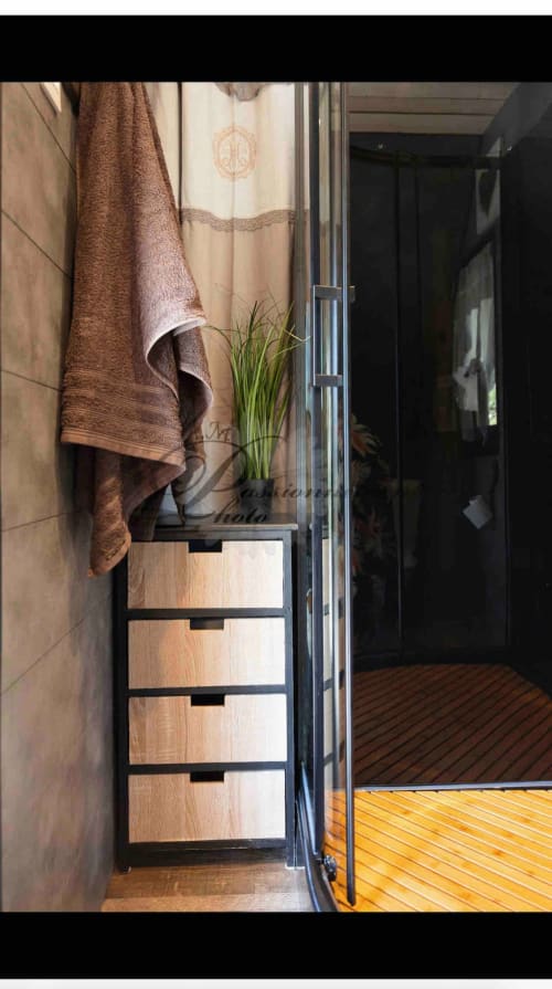 Modern bathroom entrance at Les Cabanes des Marchous cottage with wooden storage drawers, brown towels, and glass shower door