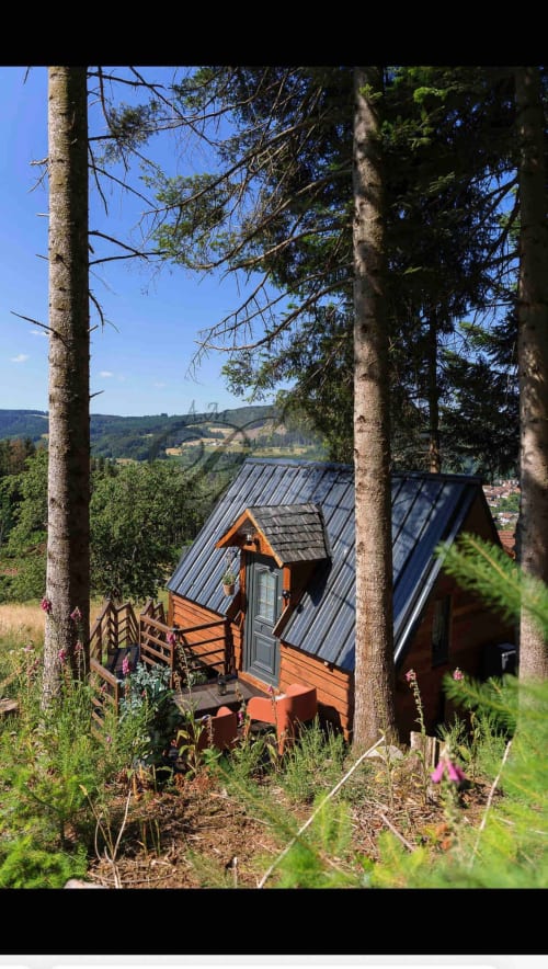 Cozy wooden cabin L'Écureuil nestled among trees with metal roof, deck, and valley views at Les Cabanes des Marchous in