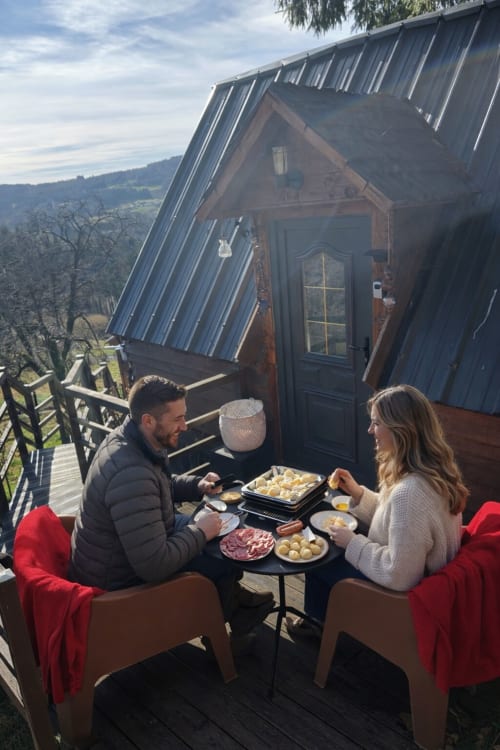 Couple dining on the deck of a mountain cabin at Les Cabanes des Marchous in France, with countryside views below