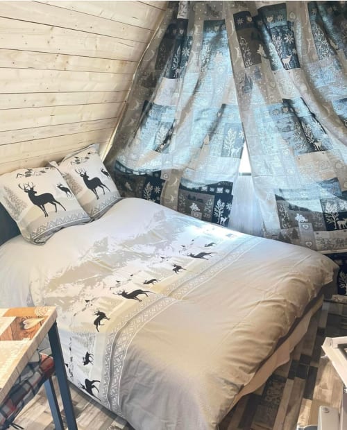 Cozy bedroom with deer-print bedding and nature-themed curtains in Cabane L'Écureuil cottage at Les Cabanes des Marchous,