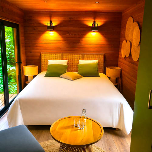 Luxus-Schlafzimmer mit Holzwänden, grünen Akzenten, weißer Bettwäsche und Gartenblick in den Lodges de Vaugrigneuse
