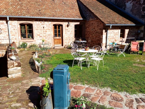 Cour de la Paulusmühle à Soucht avec maison en pierre, mobilier de bistrot blanc et jardins en fleurs