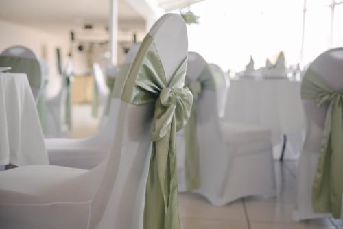 White chair covers with sage green sashes in event space at Le Domaine De La Marnière, Villainville
