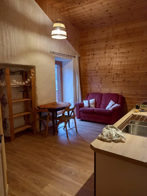 Intérieur cosy du gîte Eco Mandala : murs en bois, canapé bordeaux, table à manger, kitchenette et vue sur les montagnes