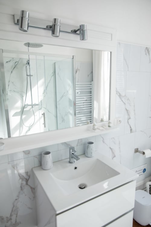 Salle de bain moderne au Château Du Landin avec murs en marbre, vasque blanche et grand miroir