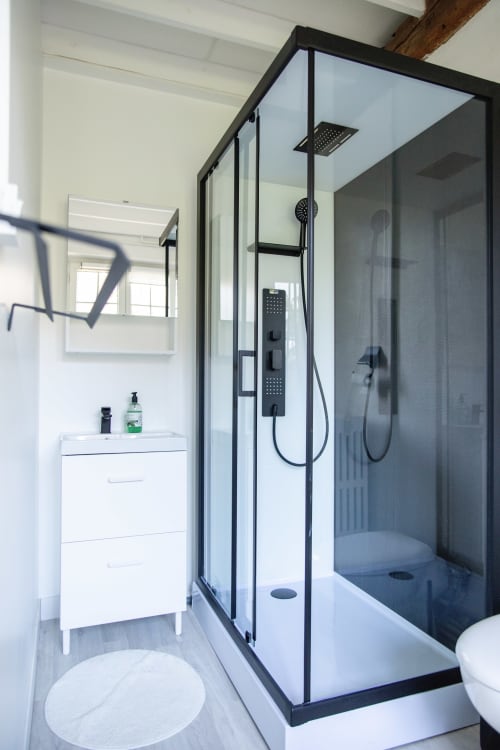 Salle de bain moderne avec douche vitrée à cadre noir, vasque blanche et toilettes à la villa Château Du Landin