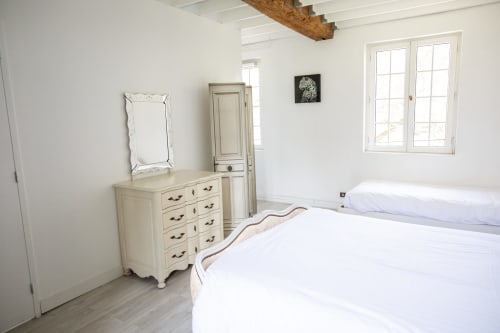 Chambre lumineuse à la villa Château Du Landin avec lits jumeaux, commode crème, miroir, plafond à poutres apparentes et vue sur le jardin