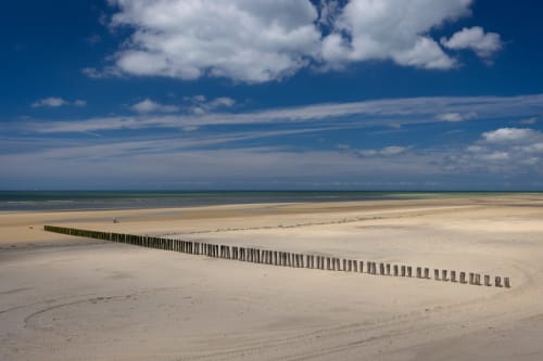 Plage de sable fin avec épis en bois s'étendant dans une mer turquoise sous ciel bleu près d'Angres, France