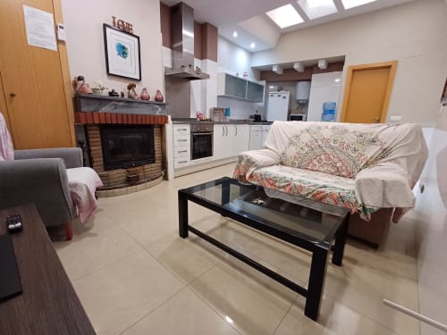 Open-plan living area at Algemesi Home apartment with fireplace, sofa, black coffee table, and equipped kitchen in background