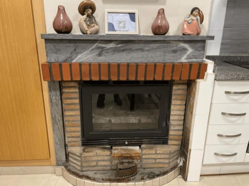 Modern fireplace with orange brick trim and grey marble mantel in Algemesi Home apartment, decorated with ceramic pottery and