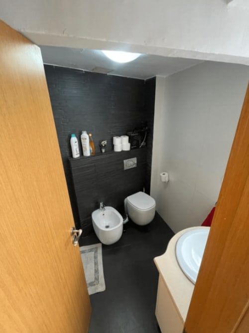 Modern bathroom at Algemesi Home apartment with black tiled walls, white bidet and toilet, pedestal sink, and storage shelf