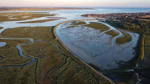 Vue aérienne des marais tidalux et cours d'eau sinueux près d'Angres, France avec ville côtière au loin
