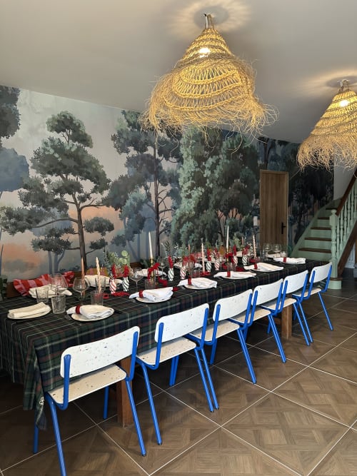 Salle à manger élégante du Mas de la Vernède avec table long, chaises bleues, luminaires suspendus tressés et décor mural forêt