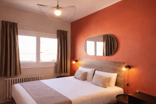 Modernes Hotelzimmer im Hôtel Des Cèdres in Orleans mit orangefarbener Akzentwand, Holzbett, rundem Spiegel und Stadtblick