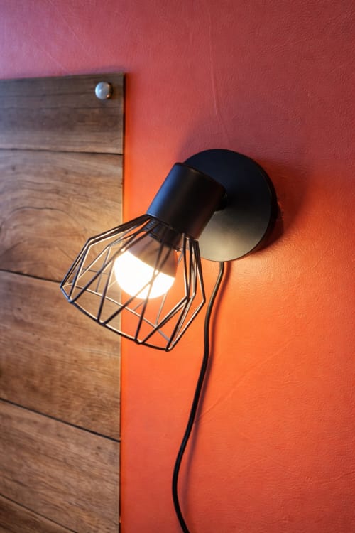 Moderne schwarze Wandleuchte mit Drahtkäfigschirm, leuchtend an einer korallenroten Wand im Hôtel Des Cèdres Orleans