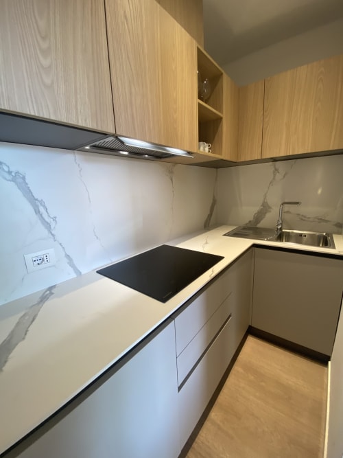 Modern kitchen in Rimini hotel with white marble backsplash, wooden cabinets, induction cooktop, and stainless steel sink