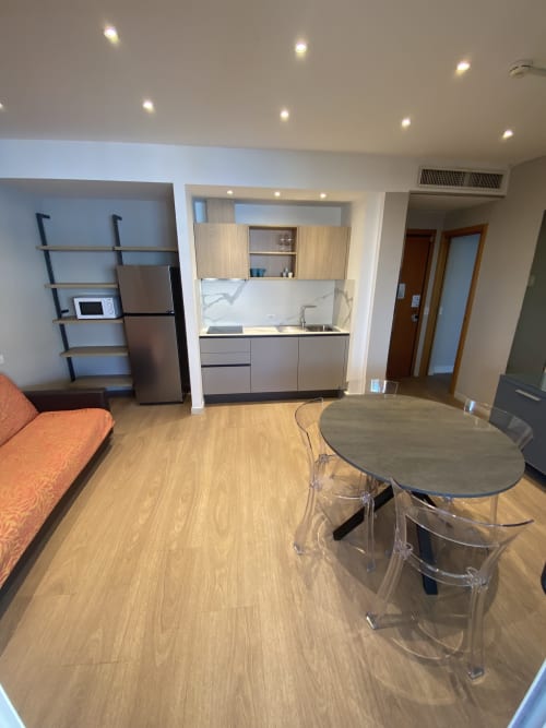Modern studio apartment at Residence Aida Rimini with kitchenette, dining table, and orange sofa on wooden flooring