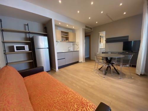 Moderna camera d'hotel presso Residence Aida Rimini con zona living, angolo cottura, tavolo da pranzo e divano arancione