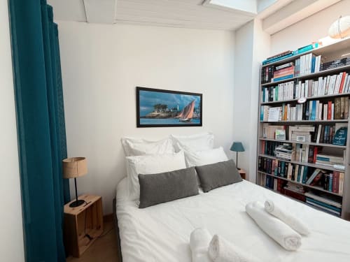Chambre cozy à la Maison ARLOÉ à La Rochelle avec literie blanche, coussins gris, rideaux bleu canard et décor marin