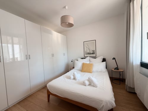 Chambre moderne à la Maison ARLOÉ à La Rochelle avec lit blanc, coussin jaune, armoire en bois, suspension et décor épuré