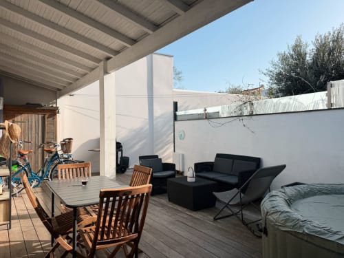 Spacieux patio de la villa Maison ARLOÉ à La Rochelle avec table de repas, canapé noir, mobilier extérieur et Jacuzzi privé