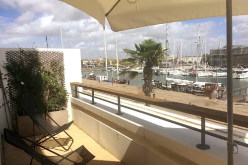 Terrasse ensoleillée de la Maison ARLOÉ à La Rochelle avec vue sur les voiliers et la marina, mobilier de jardin sous parasol