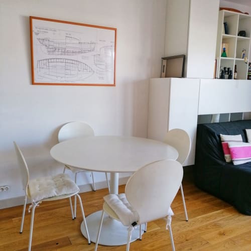Table de salle à manger blanche moderne avec chaises dans l'appartement Le Chalutier à la Maison ARLOÉ, La Rochelle, décorée d'une fresque de plans de bateau.