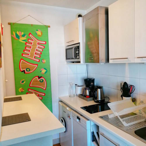 Cuisine moderne de l'appartement Le Chalutier à La Rochelle avec œuvres d'art colorées de poissons, cafetière et espace culinaire équipé