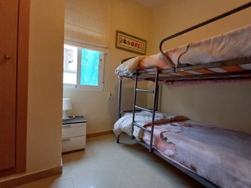 Bunk bed dorm room at Algemesi Home with metal frame beds, yellow walls, window with city view, and tile flooring