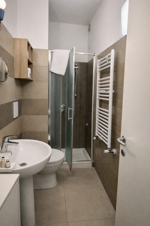 Modern bathroom in Milan garden apartment with shower, sink, toilet, heated towel rack, and wood cabinetry
