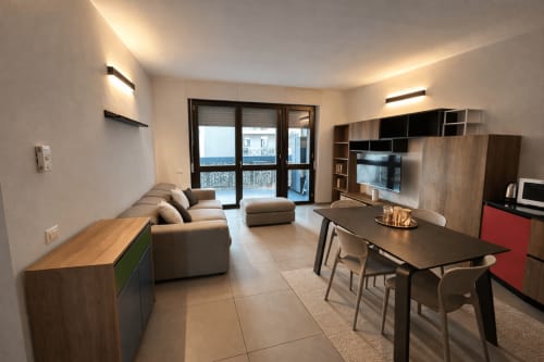 Modern Milan apartment with open-plan living, dining area, flat-screen TV, and balcony with garden view