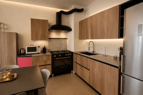 Modern kitchen in Milano apartment with wood cabinetry, black stove, island sink, and ambient lighting