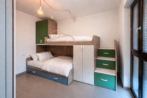 Modern loft-style bedroom with bunk beds, green accents, and wooden furniture in Milano apartment