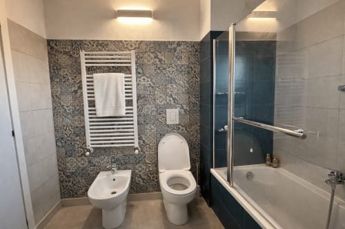 Modern bathroom in Milano apartment with bidet, toilet, white towel warmer, patterned tile backsplash, and glass-enclosed