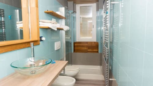 Modern bathroom at Versilia Panoramic Luxury with turquoise tiles, glass shower enclosure, wooden vanity and heated towel