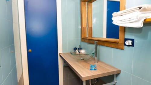 Modern bathroom at Versilia Panoramic Luxury hotel in Como, Italy with light blue tiles, wooden vanity, glass sink, and white