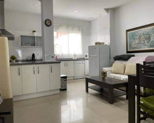 Modern open-plan apartment in Algemesí with white kitchen, black sofa, and city views from balcony