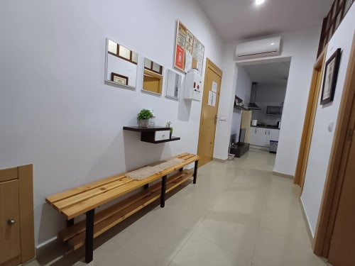 Modern apartment entryway at Algemesi Home with wooden bench, wall shelving, and access to kitchen and living areas