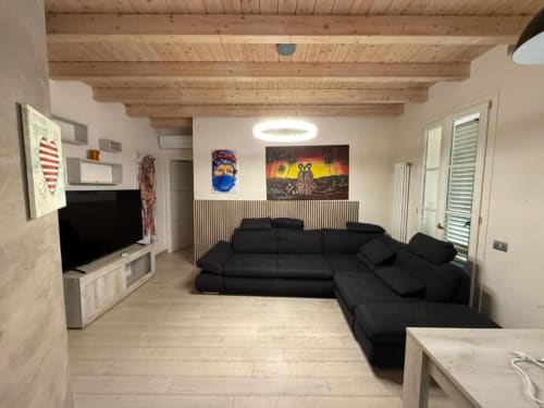 Modern living room with black sectional sofa, wooden beamed ceiling, TV, and contemporary artwork at Versilia Panoramic