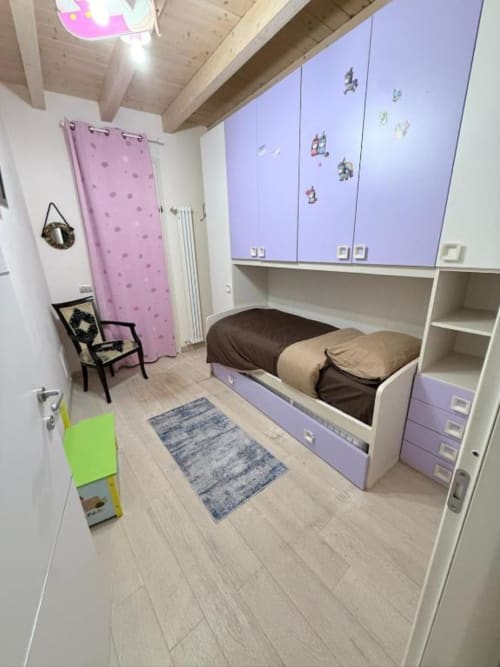 Modern child's bedroom with purple cabinetry, bed, wooden ceiling beams, and light wood flooring at Versilia Panoramic