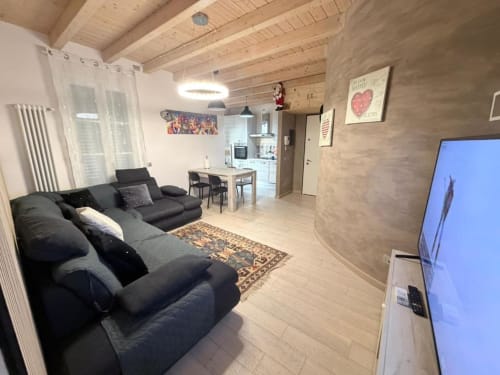 Modern Tuscan apartment living room with black sofa, wooden beams, kitchen, and TV at Versilia Panoramic Luxury, Como